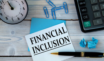 FINANCIAL INCLUSION - words on a white sheet on the background of a calculator, alarm clock and pen