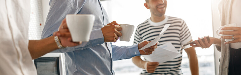 Group of diverse coworkers drink coffee during break and talking about work project