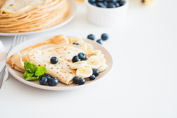 French crepes with banana and blueberries on white table. Copy space