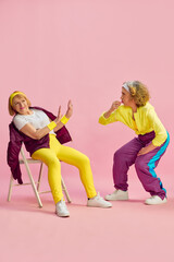 Naklejka premium Competition. Two elderly sportive women in colorful uniform training, posing against pink studio background. Concept of sportive lifestyle, retirement, health care, wellness. Ad