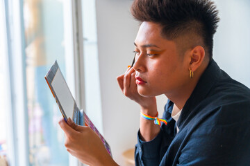 A man is applying makeup and looking at a tablet.