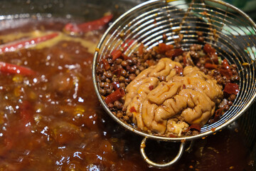 close up cooked spicy Pig's Brain on strainer above Chinese hotpot