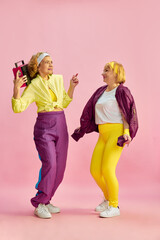 Two middle-aged, elderly, sportive woman in colorful uniform listening to radio and dancing, posing...