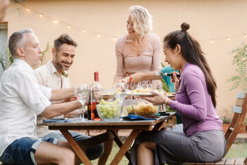 Family friends having dinner in summer, drinking wine, talking and laughing in outdoor home at night