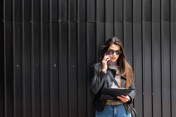 Cool Rock Businesswoman dressed in leather jacket small internet company owner standing outdoor corporate building. Female business person with sunglasses on city street near office building