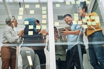 Technology saves the day again. a group of businesspeople applauding a colleague while brainstorming on a glass wall in an office.