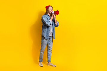 Full length photo of positive funny man wear denim screaming bullhorn emtpy space isolated yellow color background