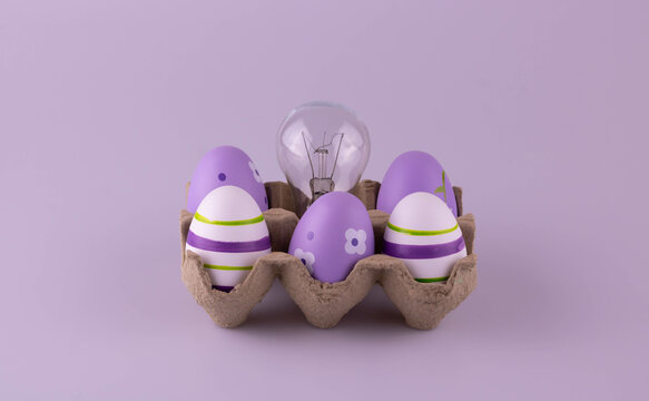 The cardboard egg container contains lilac Easter eggs and a tungsten light bulb.
