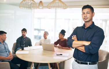 Youve got to remain firm as the boss. Portrait of a young businessman standing in an office with his colleagues in the background.