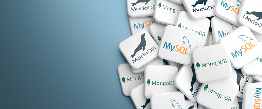 Logos of the open source / source available database systems MySQL, MariaDB and MongoDB on a heap on a table. Web banner format, copy space.