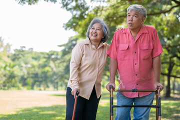 An old elderly Asian man uses a walker and walks in the park with his wife.  Concept of happy retirement With Love and care from family and caregiver, Savings, and senior health insurance