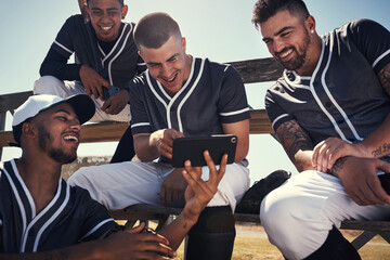 Wifi is everywhere, even at the ballpark. a group of young men using a smartphone after playing a baseball game.