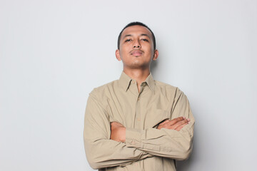 Portrait of confident smiling Asian young man wearing cream shirt standing with arms folded isolated on white background.