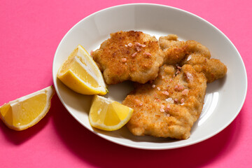 Classic fried Wiener Schnitzel served with lemon on a white plate. Breaded fried meat. A traditional dish of Austrian or German cuisine. Close-up. Copy space