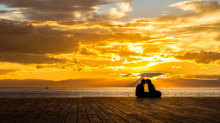 silhouette of a couple in love, sitting on a pier in sunset