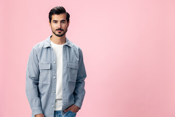 Fototapeta premium Portrait of a stylish brunette man with a beard beautiful smile on a pink background in a white T-shirt and jeans smile and joyful emotion on his face, copy space