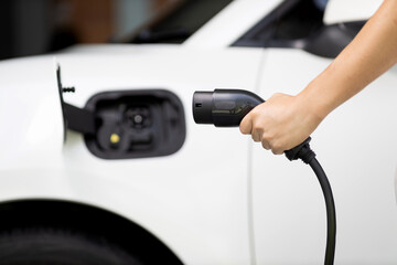 Focus hand holding EV charger plug with blurred background of progressive electric vehicle and...