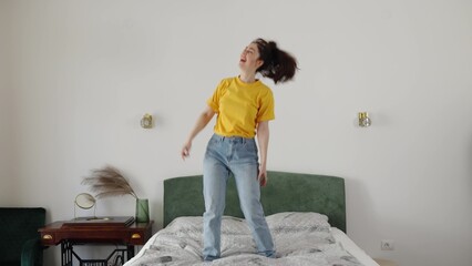 Happy young Caucasian woman funny dancing on bed wearing jeans and yellow shirt. Concept of freedom and holiday. © _KUBE_
