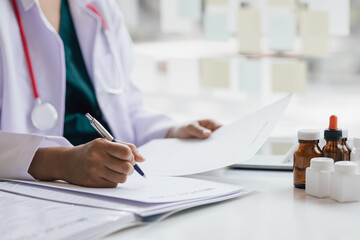 Female doctor working in a hospital is checking patient history and writing a prescription in the doctor's office.