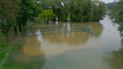 AERIAL: Volleyball court in park by the river is flooded with muddy flood water