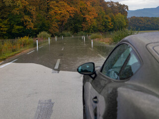 Car stopped due to a flooded part of paved roadway after heavy rains in autumn