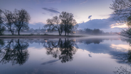 Fototapeta na wymiar Impressively beautiful fabulous morning on the river at blue hour. The rising sky is reflected in the river during a foggy morning. Panoramic view of the beautiful mystical lake.
