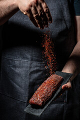 Chef hands cooking meat steak and adding seasoning in a freeze motion. Fresh raw Prime Black Angus...