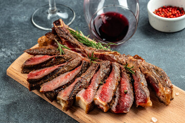 Sliced medium rare grilled steak with red wine on cutting board with rosemary and spices