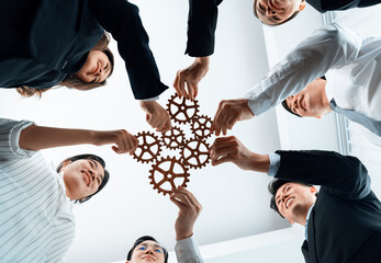 Hand holding wooden gear by businesspeople wearing suit for harmony synergy in office workplace....