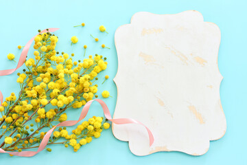 Top view image of spring yellow mimosa flowers composition over pastel blue background
