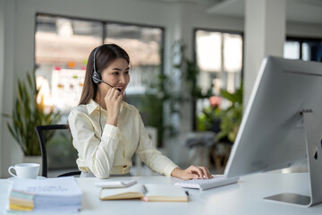 Fototapeta premium Portrait of happy smiling female customer support phone operator at workplace. Smiling beautiful Asian woman working in call center