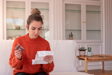 Focused woman examining drug package leaflet for prescribed medicine while sitting at home holding...