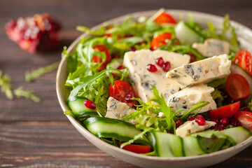 Vegetable salad with blue cheese and pomegranate grains on a wooden background