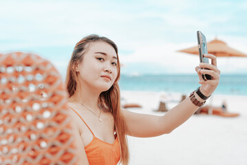 A vain asian lady in her twenties taking a selfie while at beach. Staying at a nice beachfront resort.