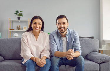 Portrait of happy couple looking and smiling at camera making video call together sitting on couch at home chatting with friends online at webcam. Concept of video call, internet connection.