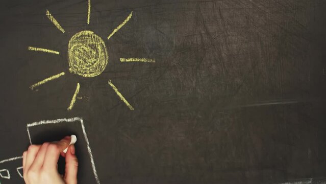Hand-drawn drawing depicting the sun in the sky over the city. The sun with rays and many high-rise houses next to each other drawn by the hand with chalk on a blackboard in timelapse