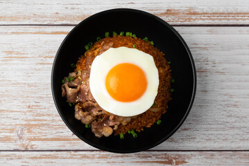 Top view of Kimchi rice with grilled brisket sliced and fried egg in black bowl on wooden table.