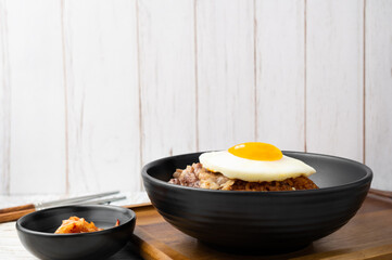 Closeup of Kimchi rice with grilled brisket sliced and fried egg in black bowl on wooden table.