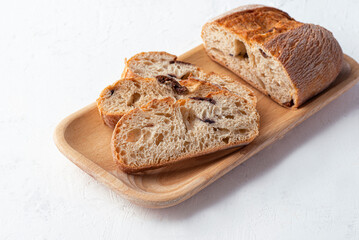 Italian Ciabatta bread with olives on a wooden tray, white table. Authentic rustic bread