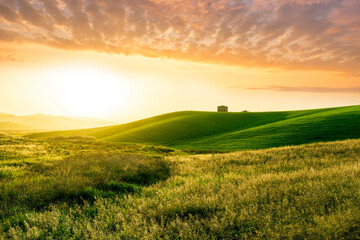 countryside sunset in green hills of spring fields with old castle farm and mountains on background of evening landscape