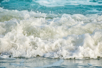 Obraz premium Close-up of the sea wave with the foam surging on the shore. View of sea water in soft focus. Background in a light blur on the theme of a serene summer vacation and relaxed vacation.