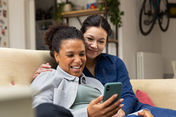 Lesbian couple using a smartphone at home together sitting on the sofa