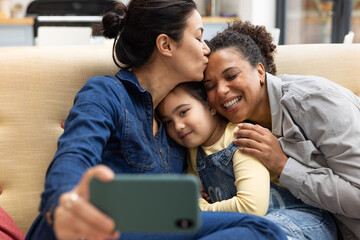 Lesbian parents taking a selfie at home with their daughter together on the sofa