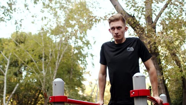 Young caucasian athlete in sportswear doing dips in an outdoor workout area close up. Sportsman doing exercises on parallel bars in the summer on a city sport ground