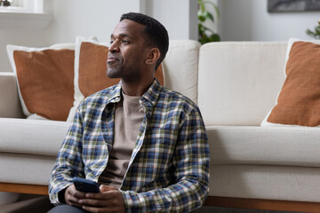 African American male at home using a smartphone and thinking