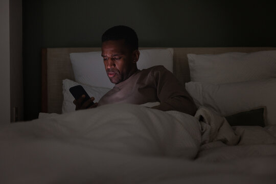 African American male using a smartphone in bed at nighttime