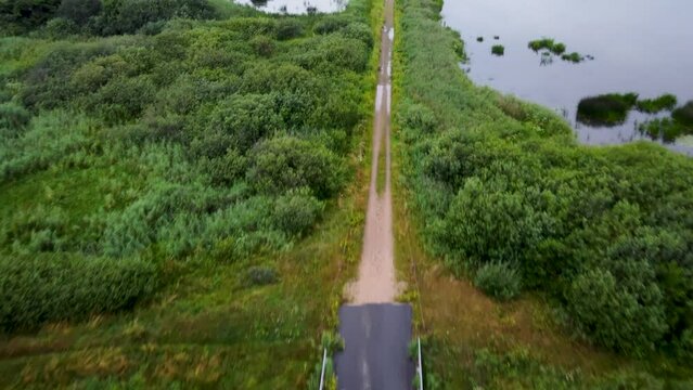 Aerial of a long road alongside water pond and swamps in Romo Denmark during the daytime