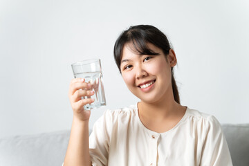 healthy beautiful young woman holding a glass of water sitting on the couch at the livingroom.