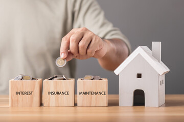 Saving money for house concept, Necessary cost for house, Man holding coin and put in wooden block on wooden desk with grey house model. Money and financial for house concept.