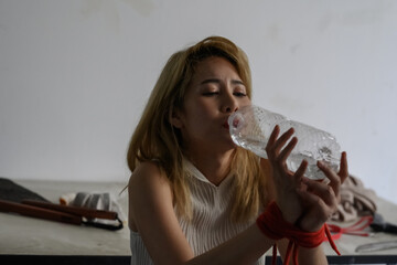 poor woman kidnapped or held hostage by being bound with a red rope was drinking water thirsty
